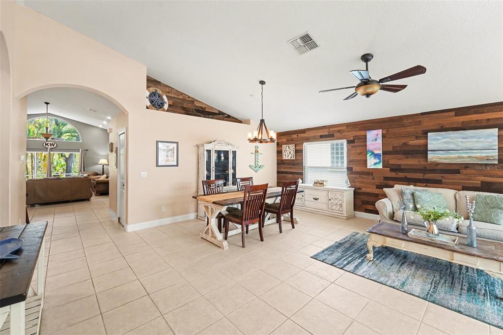 A living and dining area features tile floors, a wood-plank accent wall, and vaulted ceilings — 12324 GLENFIELD AVENUE, TAMPA, FL