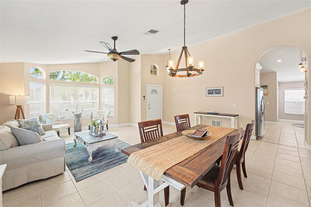 An open-concept living and dining area features tile flooring, a ceiling fan, and a chandelier — 12324 GLENFIELD AVENUE, TAMPA, FL