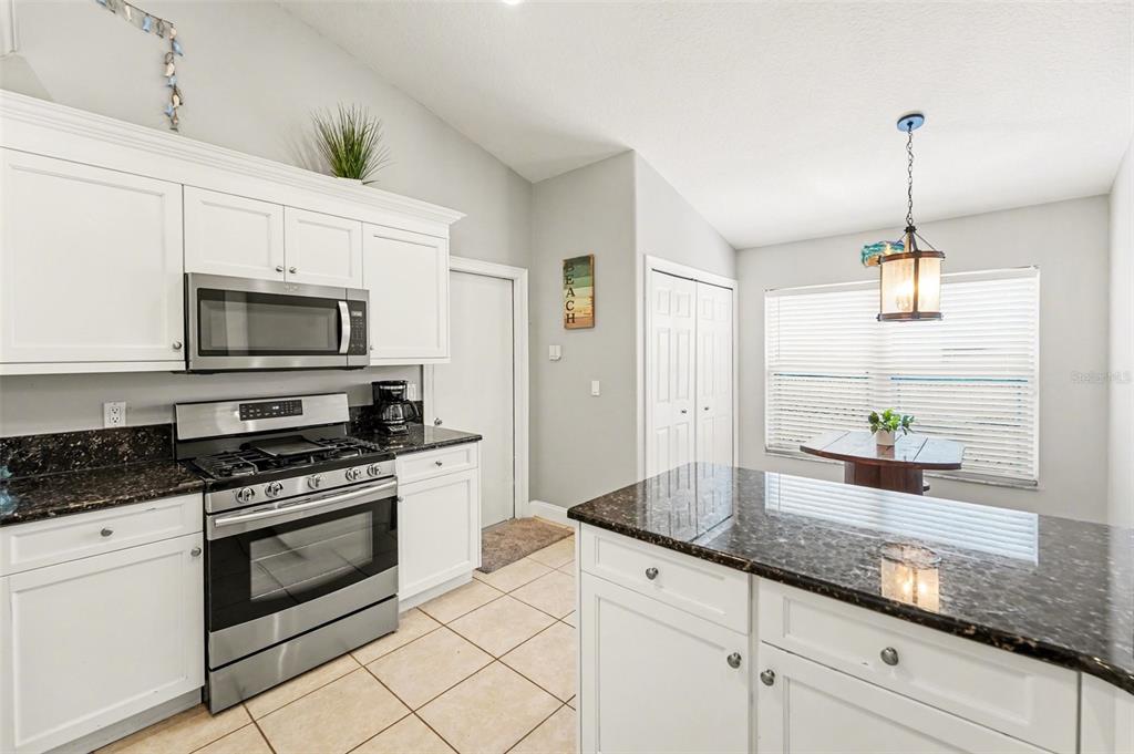 A kitchen features white cabinets, dark granite countertops, stainless steel appliances, and a dining area — 12324 GLENFIELD AVENUE, TAMPA, FL