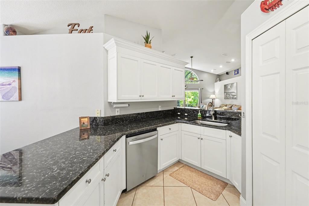 A kitchen features white cabinets, dark granite countertops, stainless steel appliances, and tile flooring — 12324 GLENFIELD AVENUE, TAMPA, FL