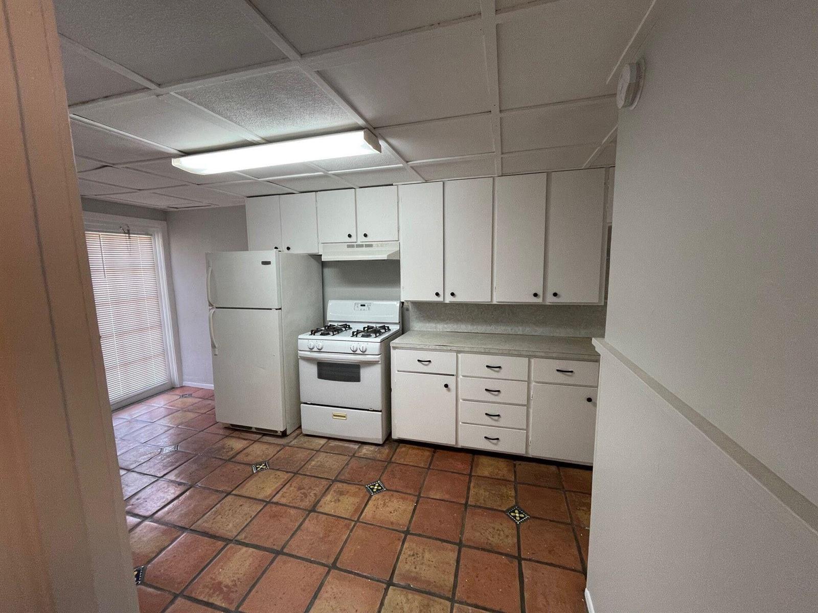 A kitchen features white cabinets, a white stove and refrigerator, and terracotta tile flooring — 736 Omar Road # 1, West Palm Beach FL 33405, WEST PALM BEACH, FL