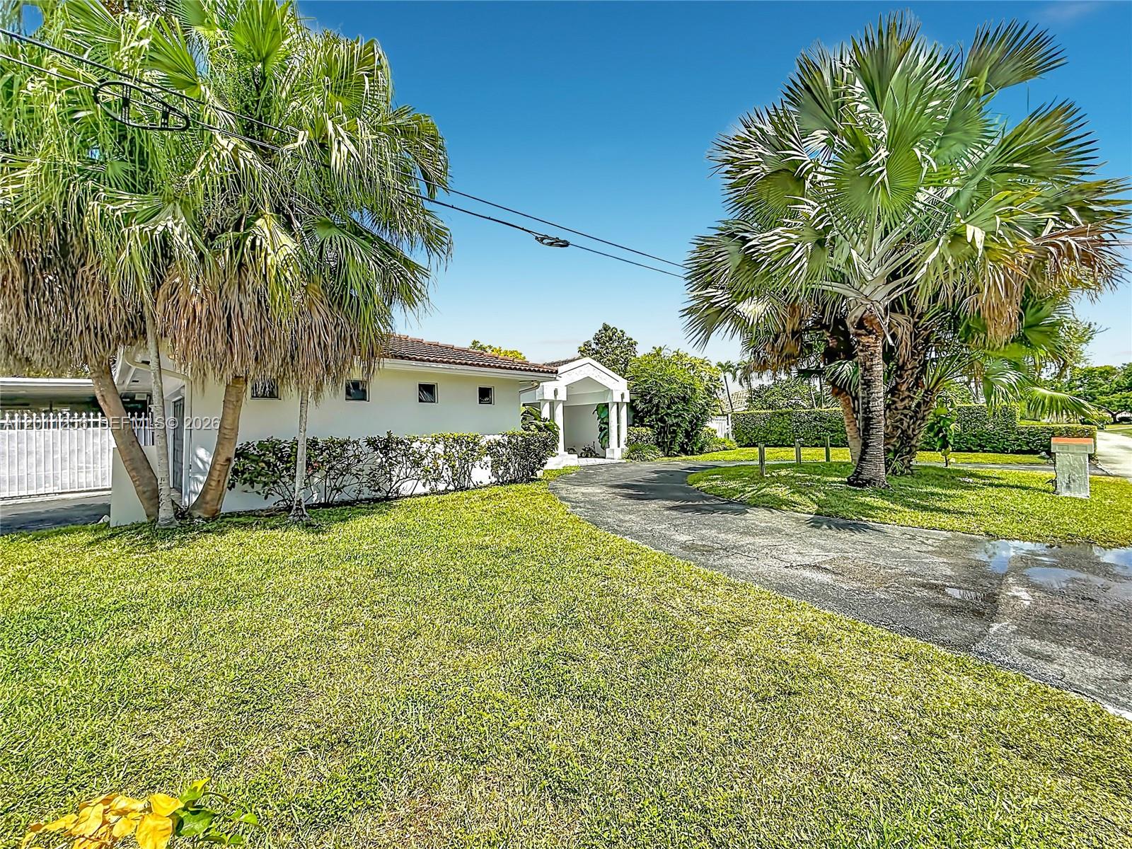 A white single-story house with a curved driveway and lush landscaping under a blue sky — 7790 SW 91st Ave, Miami FL 33173, MIAMI, FL