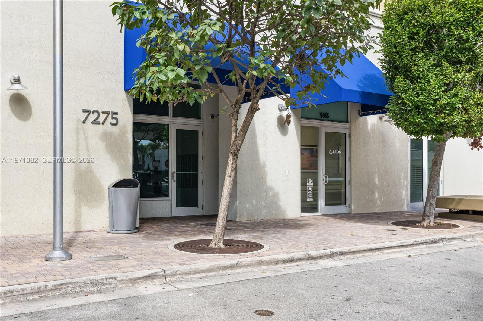 The exterior of a commercial building features two glass entry doors under blue fabric awnings — 7275 SW 90th Way # 404, Miami FL 33156, MIAMI, FL
