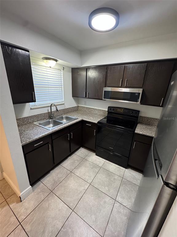 A kitchen features dark wood cabinets, granite countertops, stainless steel appliances, and tiled flooring — 1197-1197 BENTLEY ROAD UNIT 3, LEESBURG, FL