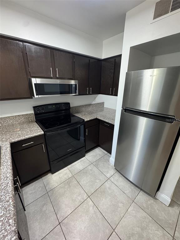 A kitchen features dark wood cabinets, granite countertops, stainless steel appliances, and light tile flooring — 1197-1197 BENTLEY ROAD UNIT 3, LEESBURG, FL