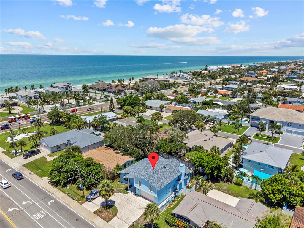 An aerial view shows a blue house with a gray roof near a coastal beach — 107 CAUSEWAY BOULEVARD, BELLEAIR BEACH, FL
