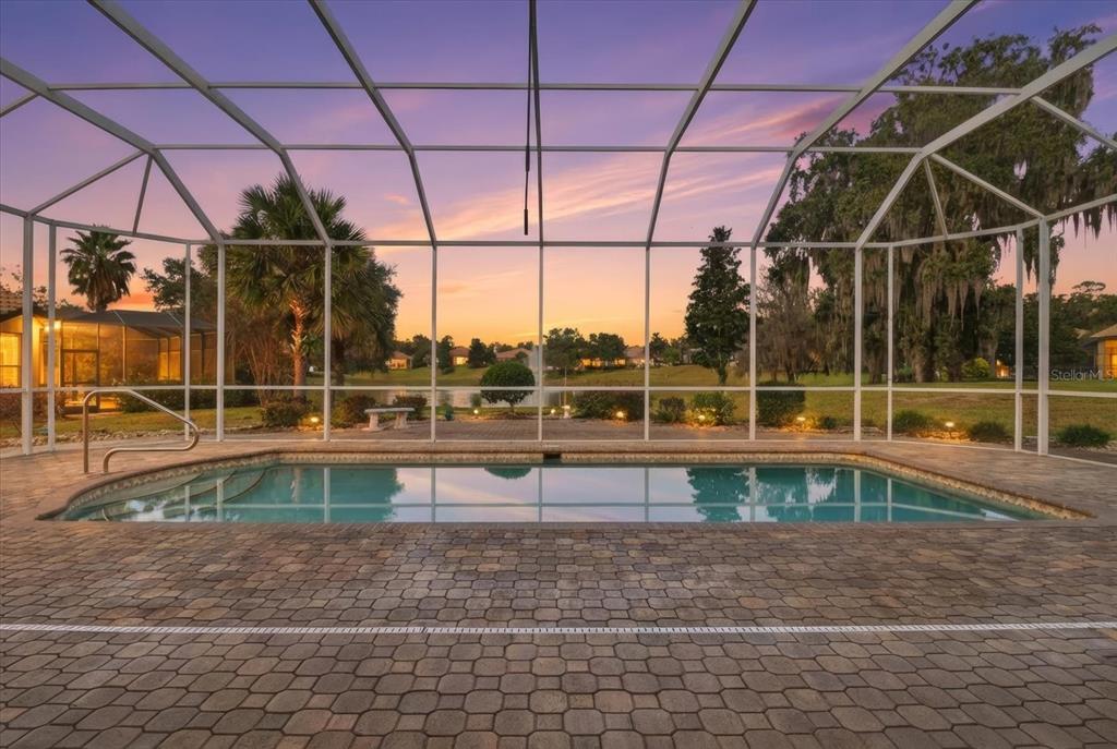 A screened-in swimming pool with a paver deck overlooks a pond at sunset — 1165 W BEAGLE RUN LOOP, HERNANDO, FL