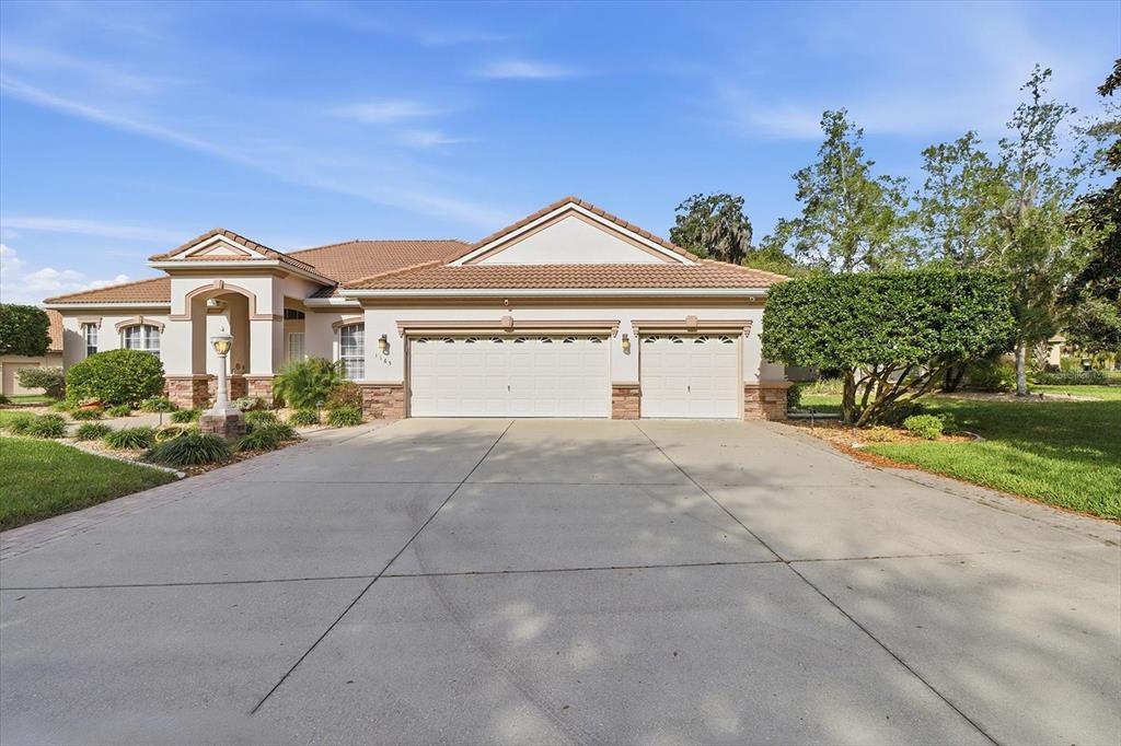 A single-story house with a three-car garage and a concrete driveway under a blue sky — 1165 W BEAGLE RUN LOOP, HERNANDO, FL