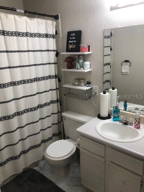 A bathroom features a patterned shower curtain, a white vanity with a sink, and wall shelving — 1025 S HIAWASSEE ROAD UNIT 2226, ORLANDO, FL