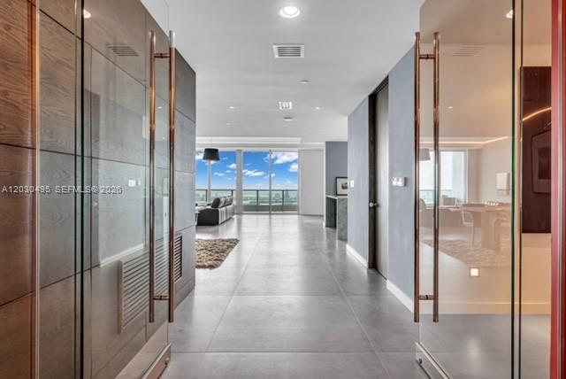 A modern hallway with large glass doors leads to an open living area with floor-to-ceiling windows — 900 Biscayne Blvd, Miami FL 33132, MIAMI, FL