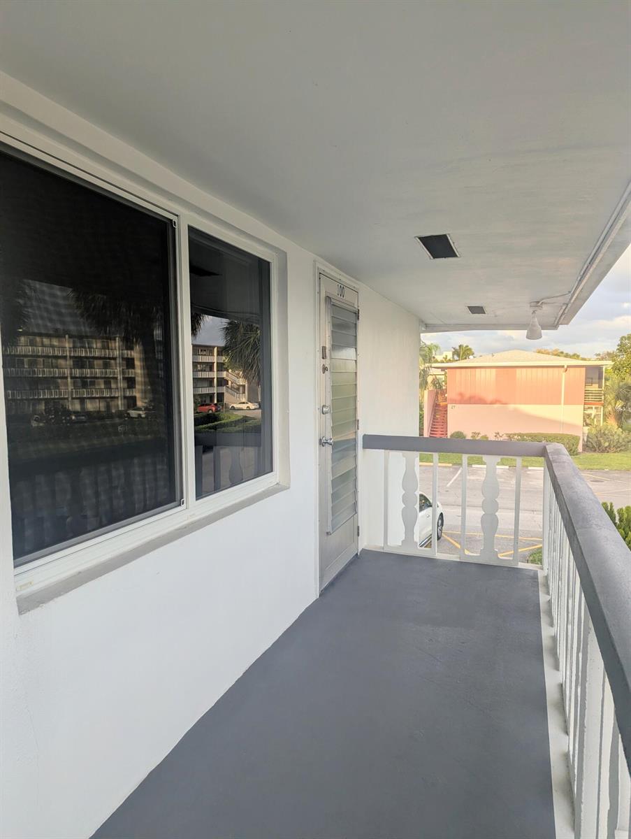 An exterior balcony with a gray floor, white railing, and a door labeled 100 — 100 Kingswood E, West Palm Beach FL 33417, WEST PALM BEACH, FL