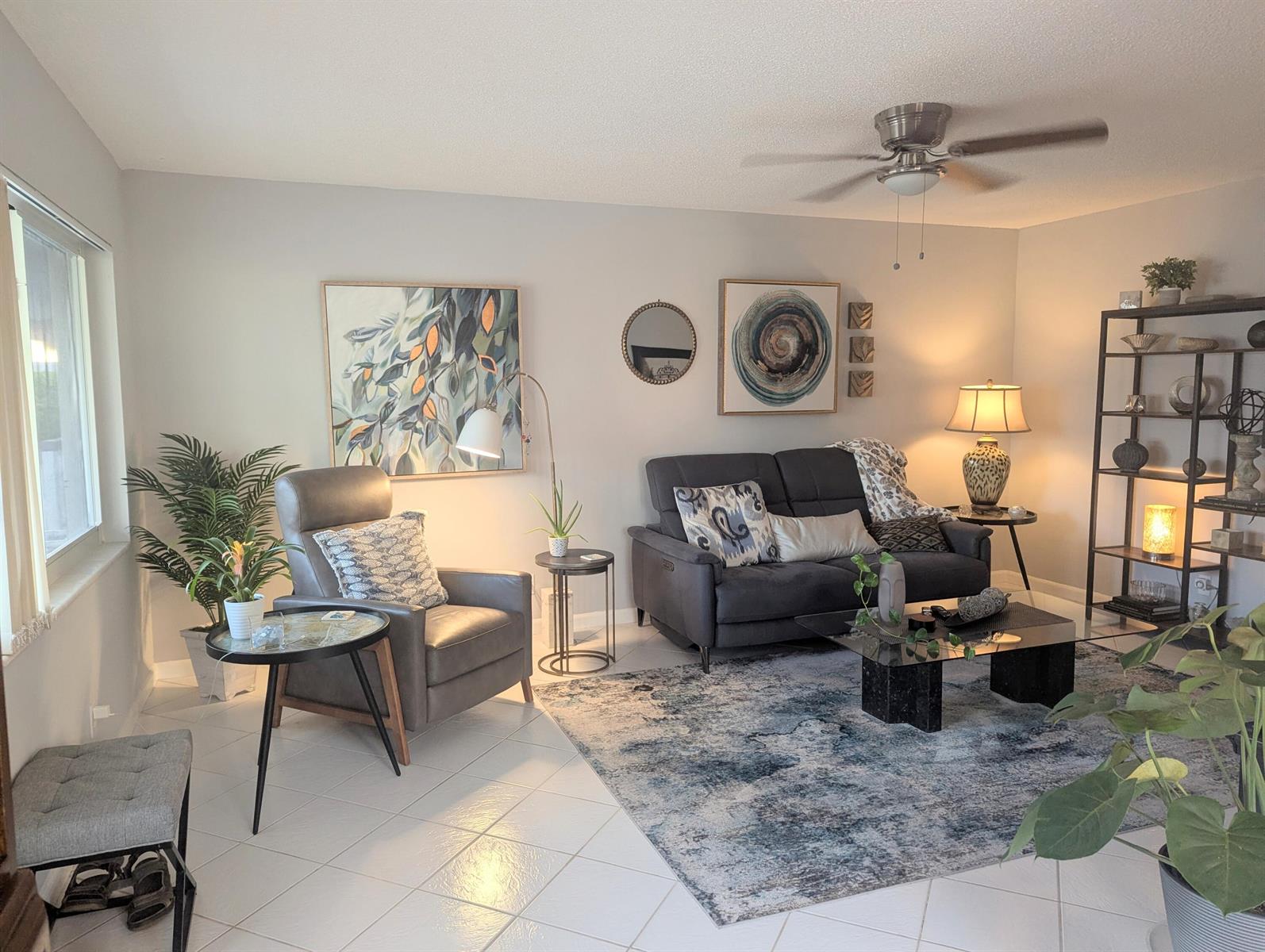 A living room features a gray sofa, an armchair, a glass coffee table, and shelving — 100 Kingswood E, West Palm Beach FL 33417, WEST PALM BEACH, FL