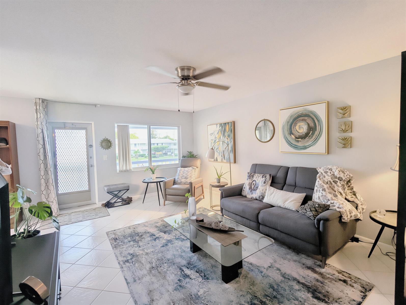 A living room features a grey sofa, glass coffee table, area rug, and ceiling fan — 100 Kingswood E, West Palm Beach FL 33417, WEST PALM BEACH, FL