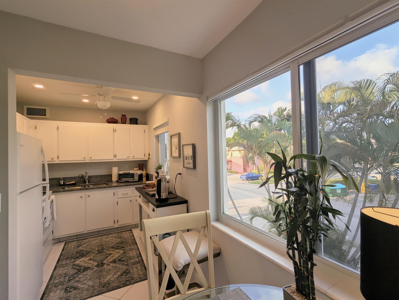 A kitchen with white cabinets and a large window overlooking palm trees and a parking lot — 100 Kingswood E, West Palm Beach FL 33417, WEST PALM BEACH, FL