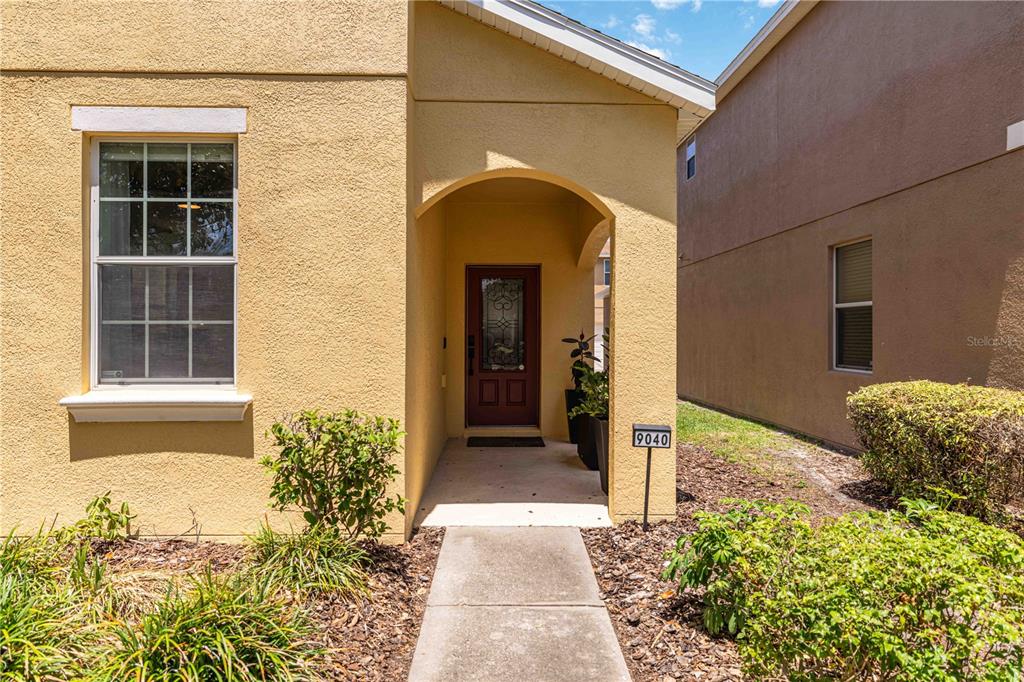 A yellow stucco house exterior features a covered entryway with a brown front door — 9040 ASPEN HOLLOW PLACE, RIVERVIEW, FL