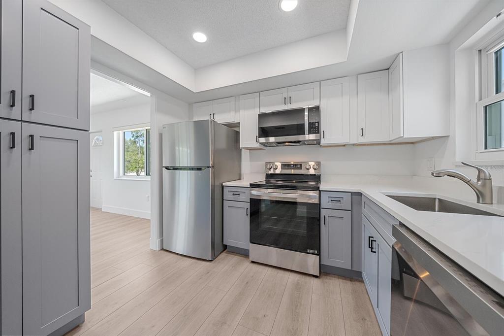 A kitchen features gray lower cabinets, white upper cabinets, stainless steel appliances, and light flooring — 3818 ROXANE BOULEVARD UNIT 157, SARASOTA, FL
