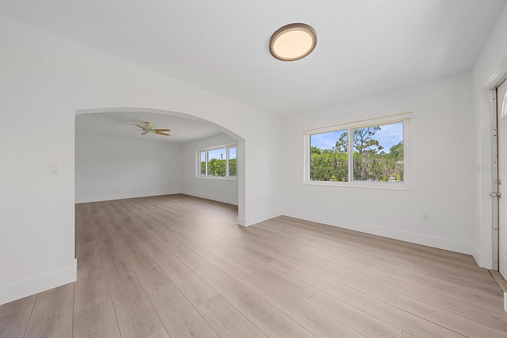 A bright, empty living area with light wood-look flooring, white walls, and an arched entryway — 3818 ROXANE BOULEVARD UNIT 157, SARASOTA, FL
