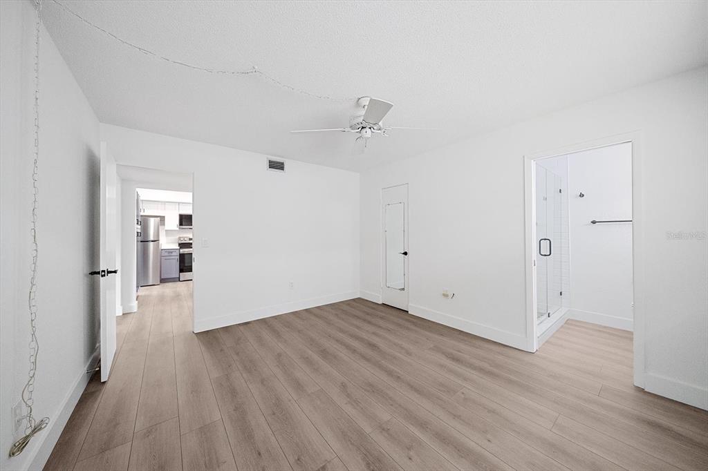 A bedroom with light wood-look flooring, white walls, a ceiling fan, and an attached bathroom — 3818 ROXANE BOULEVARD UNIT 157, SARASOTA, FL
