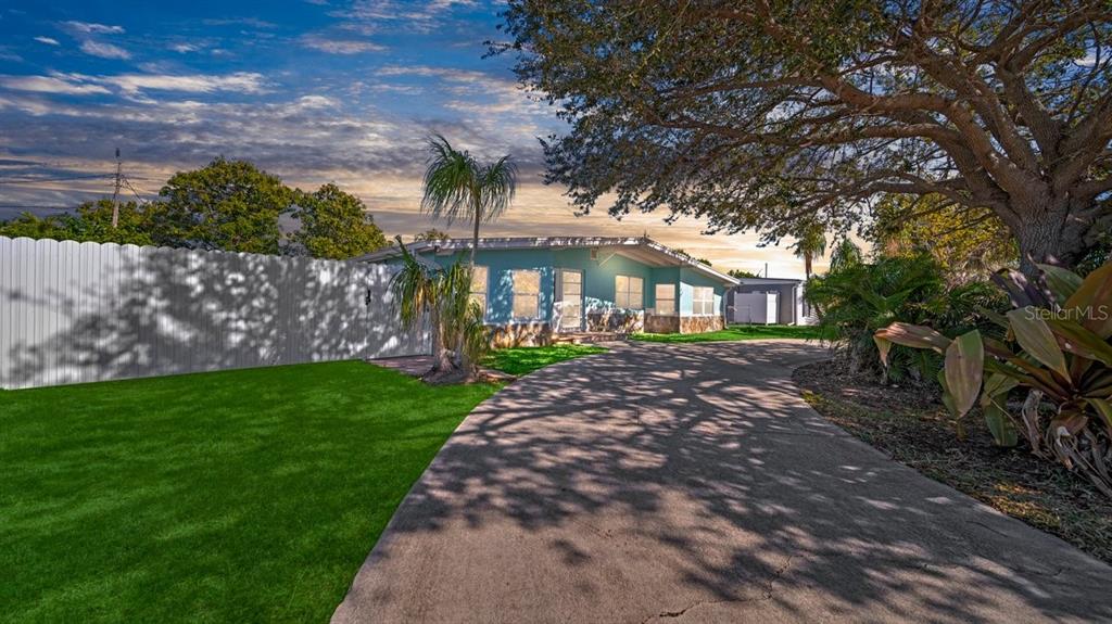 A light blue house with a concrete driveway and a large tree in the front yard — 170 POINSETTIA CIRCLE NE, PORT CHARLOTTE, FL