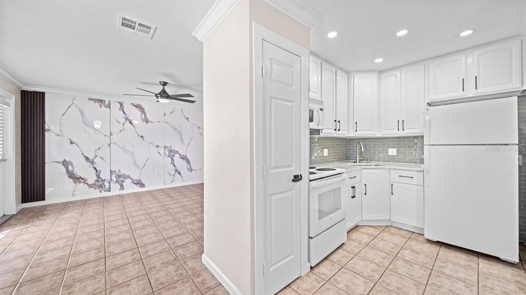 A kitchen with white cabinets and a tiled floor opens to a room with marble-patterned walls — 170 POINSETTIA CIRCLE NE, PORT CHARLOTTE, FL