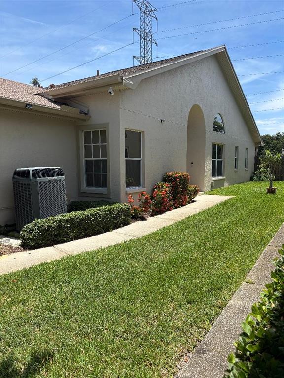A side view of a beige stucco house with a lawn, sidewalk, and HVAC unit — 3051 BROOKFIELD LANE, CLEARWATER, FL