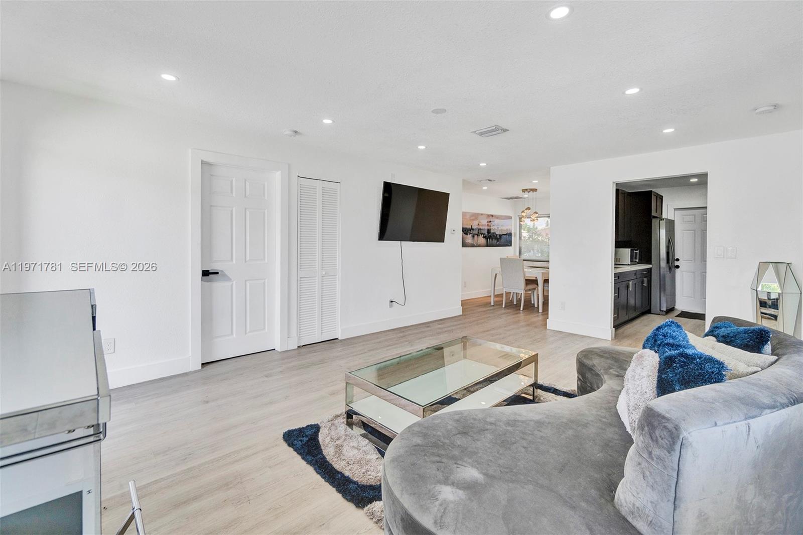 A living room features light wood-look flooring, a curved gray sofa, and a wall-mounted television — 4029 SW 22nd St, West Park FL 33023, WEST PARK, FL