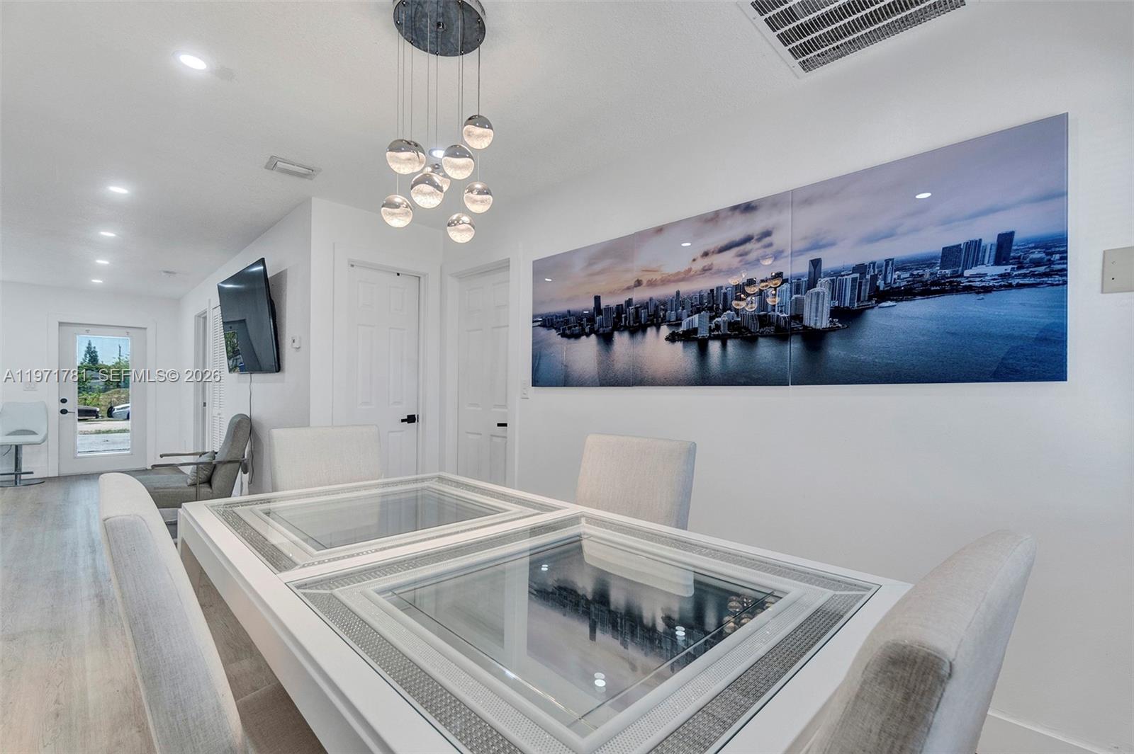 A dining room features a white table with glass insets, a modern chandelier, and wall art — 4029 SW 22nd St, West Park FL 33023, WEST PARK, FL
