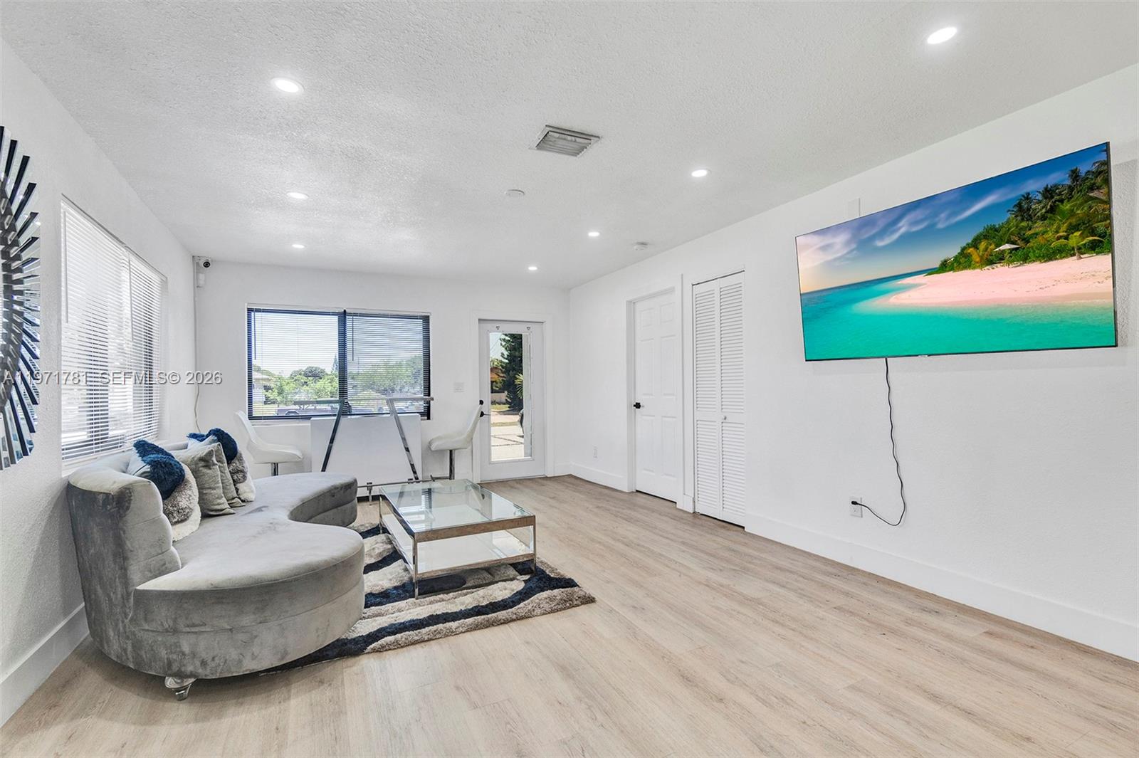 A living room features a curved gray sofa, a glass coffee table, and a wall-mounted television — 4029 SW 22nd St, West Park FL 33023, WEST PARK, FL