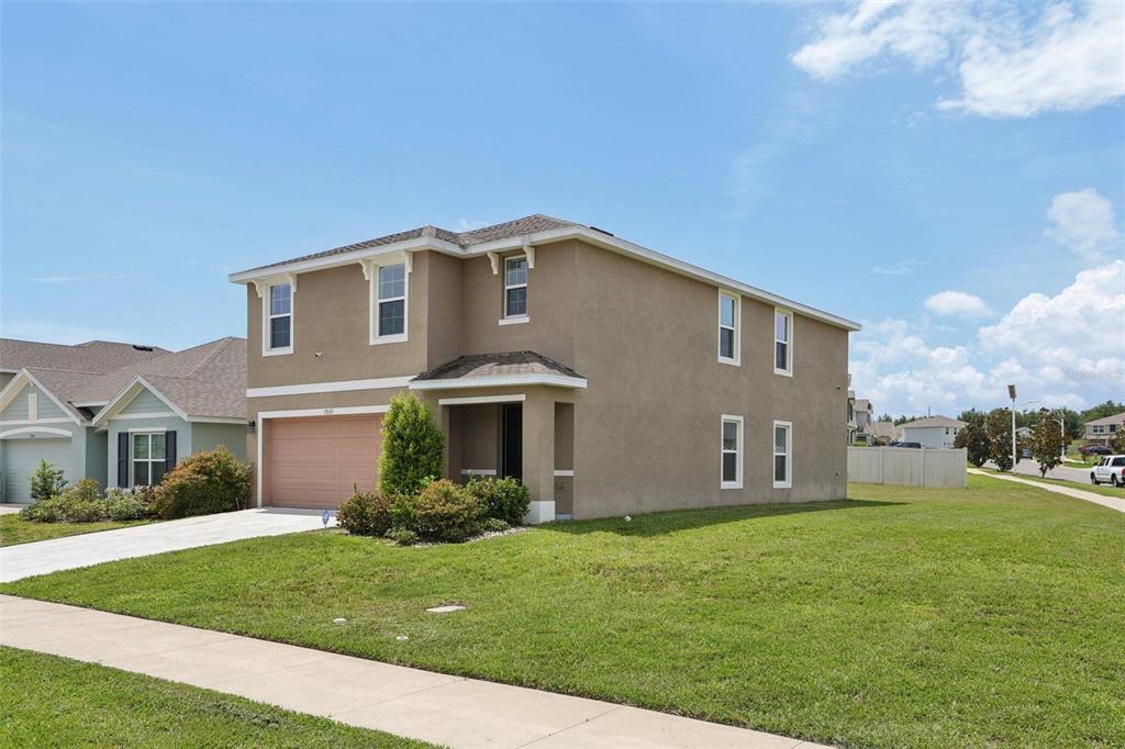A two-story tan stucco house with a two-car garage and a side yard — 7530 BROAD POINTE DRIVE, ZEPHYRHILLS, FL