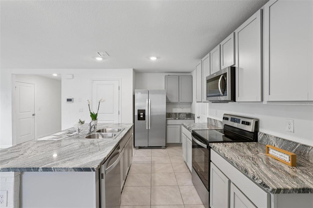 A modern kitchen features gray cabinets, granite countertops, stainless steel appliances, and a central island — 7530 BROAD POINTE DRIVE, ZEPHYRHILLS, FL