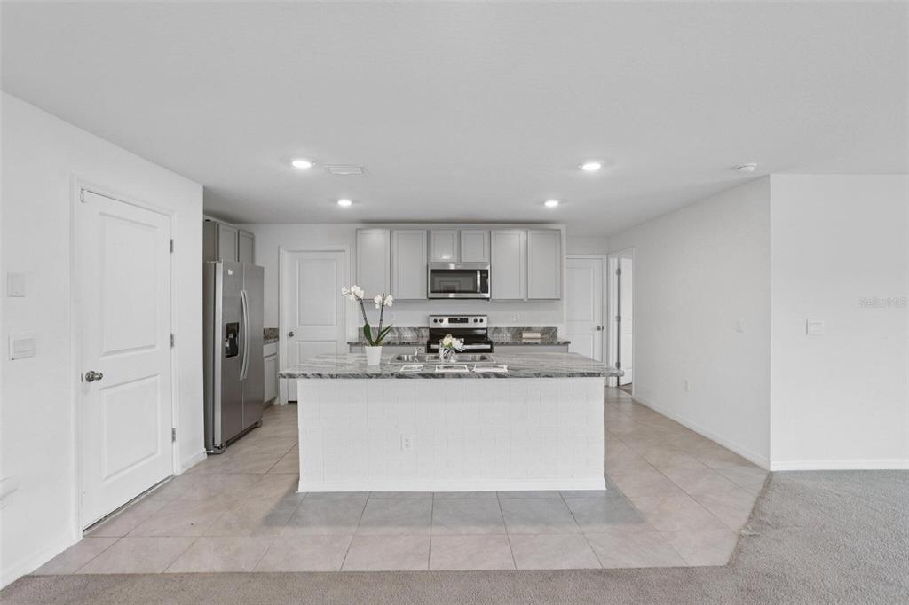 A kitchen features a central island with a marble countertop, stainless steel appliances, and cabinetry — 7530 BROAD POINTE DRIVE, ZEPHYRHILLS, FL