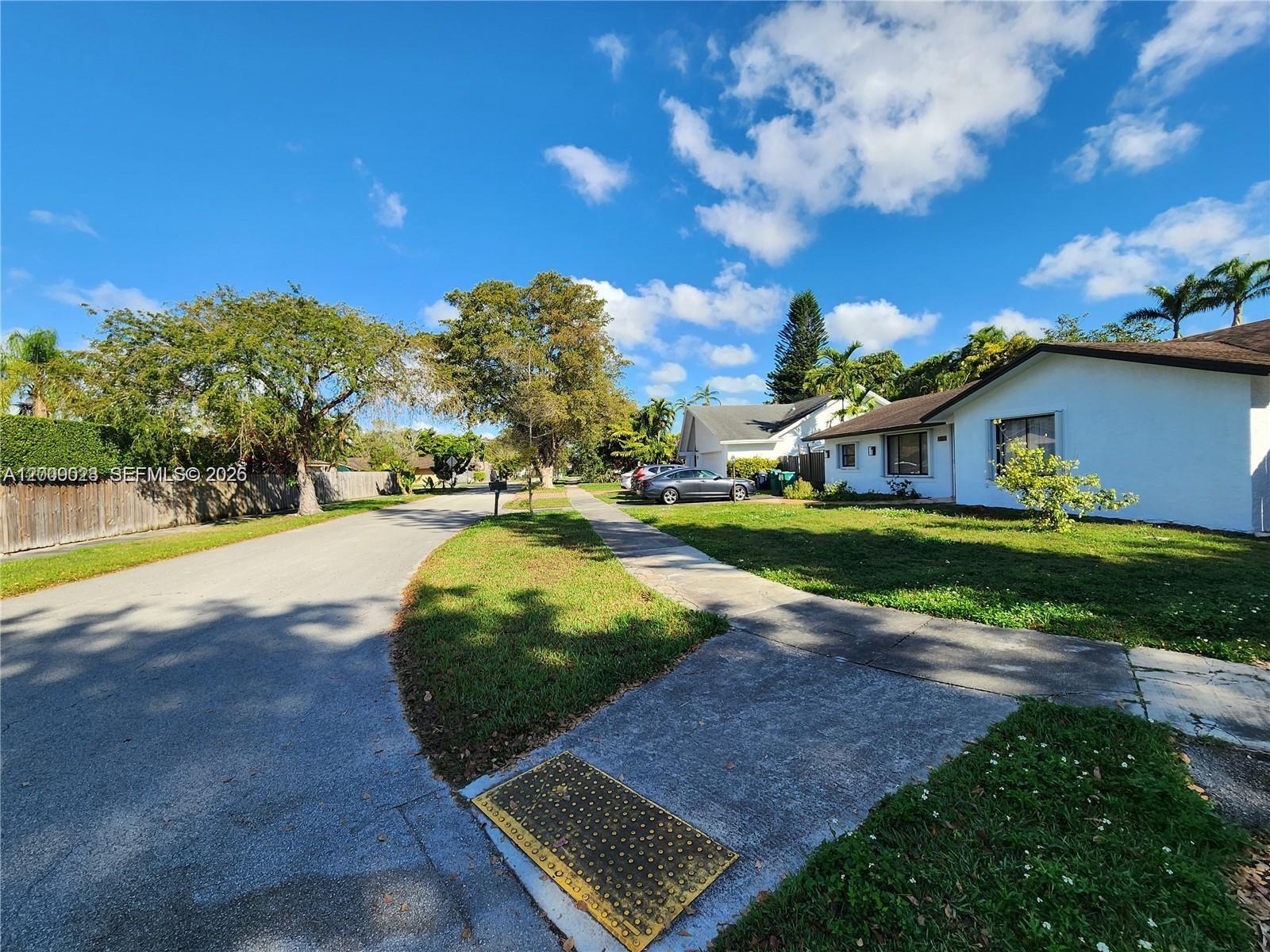 A suburban street view showing a sidewalk, a grassy lawn, and a white house — 9825 SW 132nd Ct, Miami FL 33186, MIAMI, FL