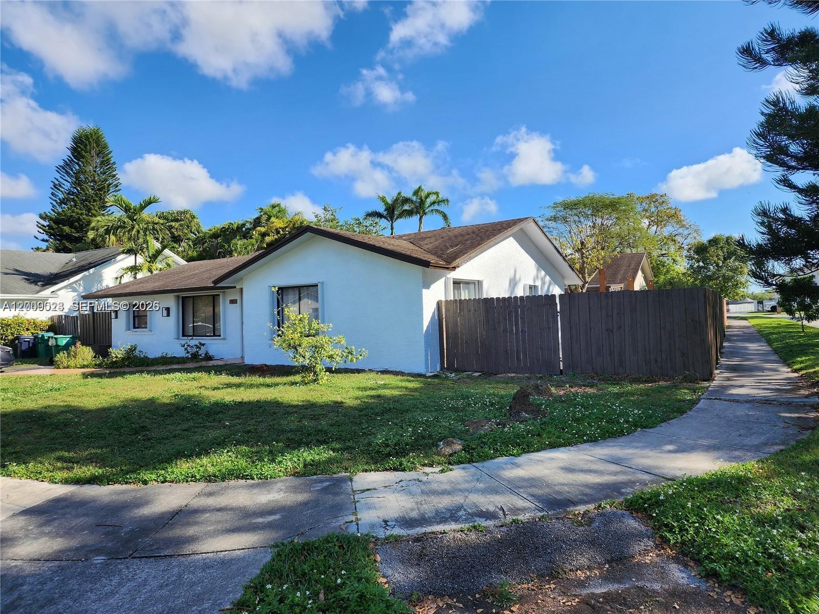 A white single-story house features a brown roof, a wooden fence, and a front lawn — 9825 SW 132nd Ct, Miami FL 33186, MIAMI, FL