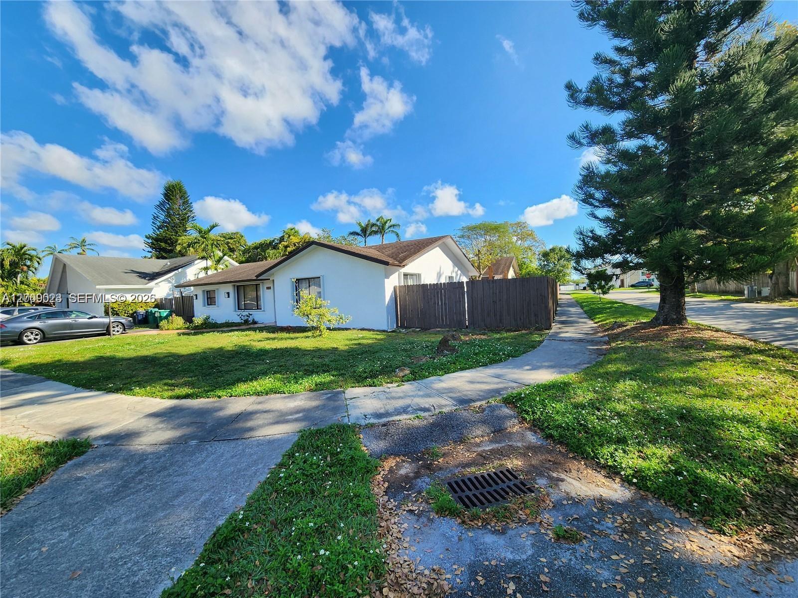 A white single-story house with a brown wooden fence sits on a corner lot — 9825 SW 132nd Ct, Miami FL 33186, MIAMI, FL