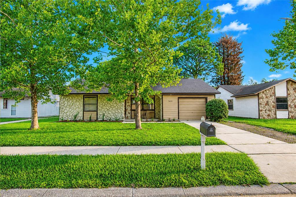 A single-story house with a stone facade, tan garage, and large trees in the front yard — 7621 RUTHWIND COURT, ORLANDO, FL