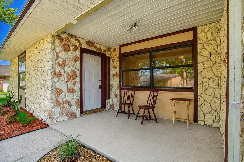A covered concrete porch features stone veneer walls, a white front door, and two wooden chairs — 7621 RUTHWIND COURT, ORLANDO, FL