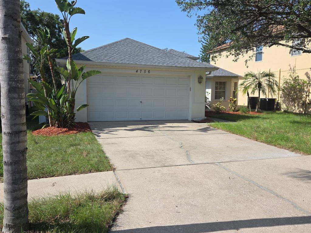 A single-story house exterior features a white garage, a concrete walkway, and a front entrance — 4756 WHISPERING WIND AVENUE, TAMPA, FL