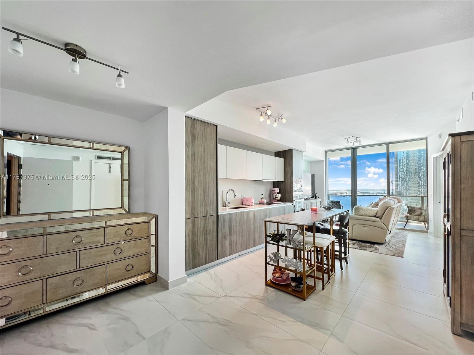 A modern kitchen and living area feature wood cabinetry, marble-look floors, and a balcony view — 2900 NE 7th Ave # 2008, Miami FL 33137, MIAMI, FL