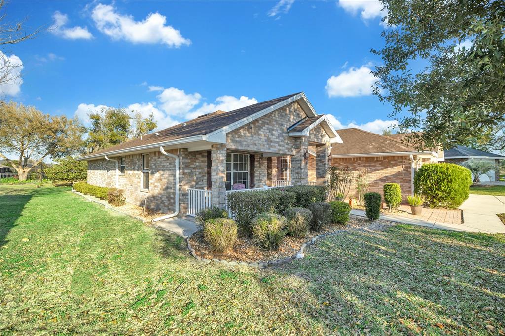 A brick house exterior features a covered front porch, a small lawn, and landscaping — 4319 SW 63RD STREET, OCALA, FL