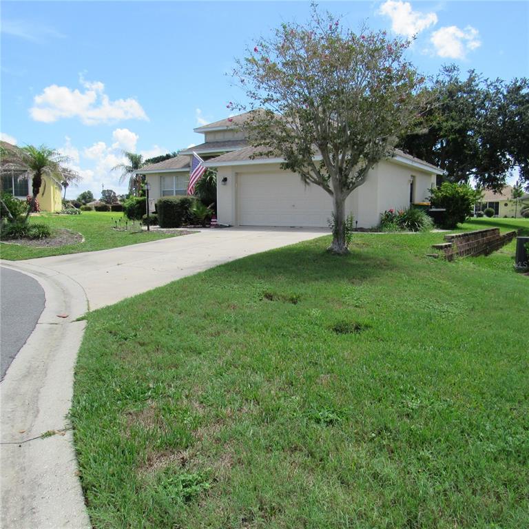 A single-story house with a two-car garage and a large tree in the front yard — 3204 ANTIGUA BAY LANE, TAVARES, FL