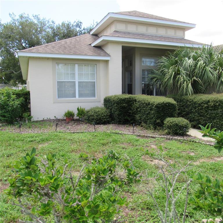A single-story house with beige stucco siding, a hip roof, and a landscaped front yard — 3204 ANTIGUA BAY LANE, TAVARES, FL