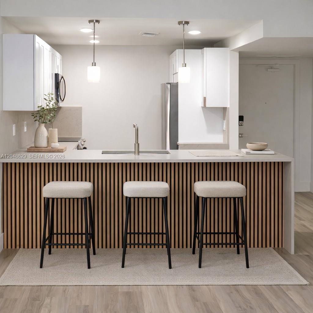 A modern kitchen features white cabinets, a slatted wood island, and three bar stools — 3080 N Course Dr # 602, Pompano Beach FL 33069, POMPANO BEACH, FL