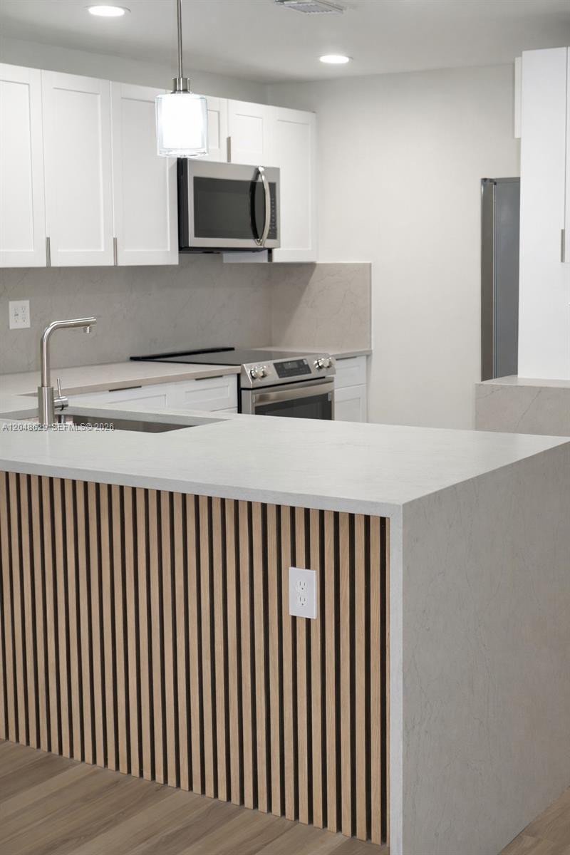 A modern kitchen features white cabinets, a stone countertop island, and wood slat detailing — 3080 N Course Dr # 602, Pompano Beach FL 33069, POMPANO BEACH, FL