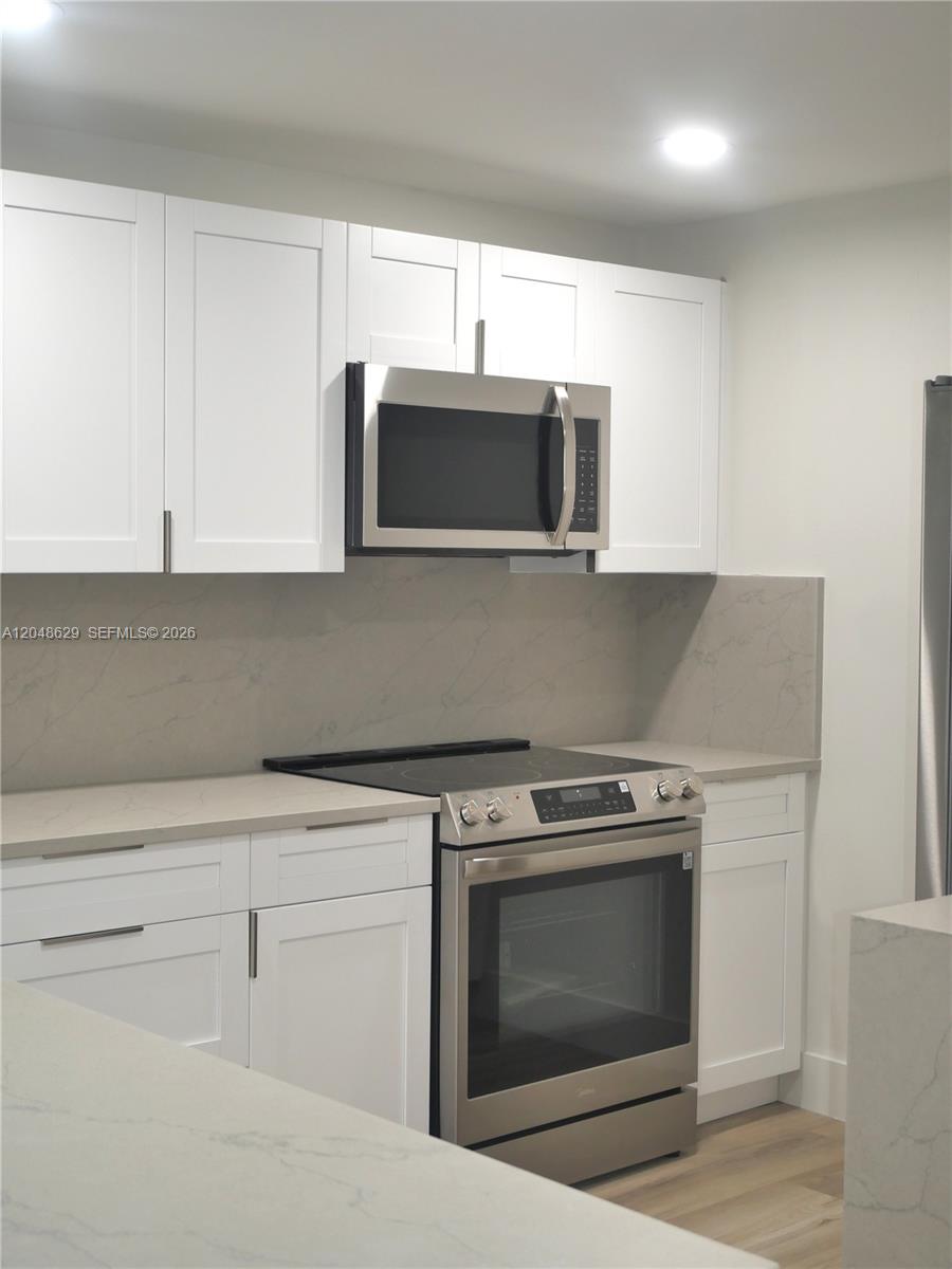 A modern kitchen features white shaker cabinets, stainless steel appliances, and light marble-patterned countertops — 3080 N Course Dr # 602, Pompano Beach FL 33069, POMPANO BEACH, FL