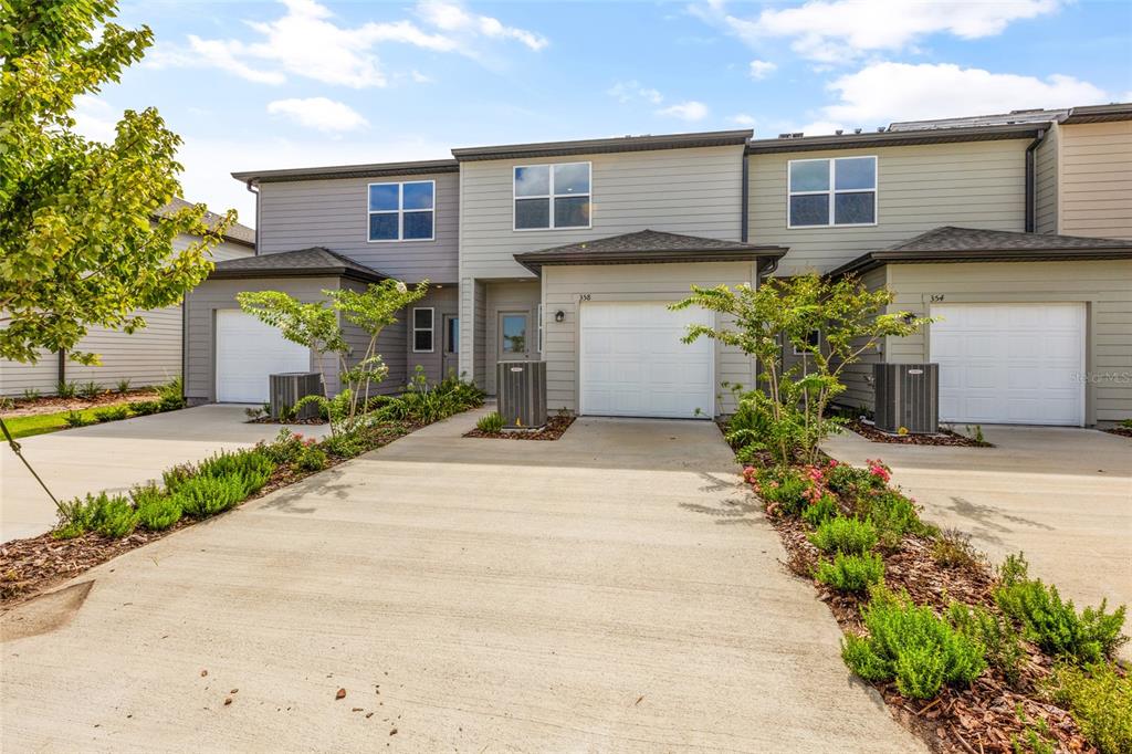 A row of three attached townhomes with concrete driveways, garages, and light-colored siding — 358 CADBERRY PLACE, ST CLOUD, FL