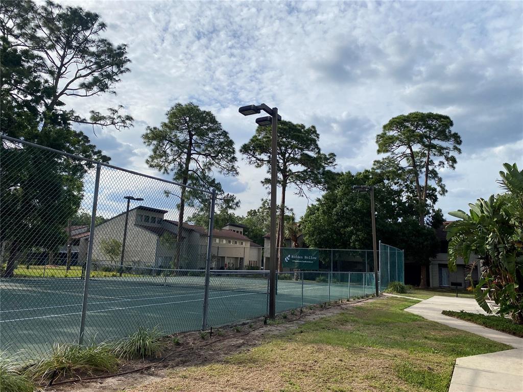 A tennis court with a chain-link fence and tall trees under a cloudy sky — 4394 SANDNER DRIVE, SARASOTA, FL