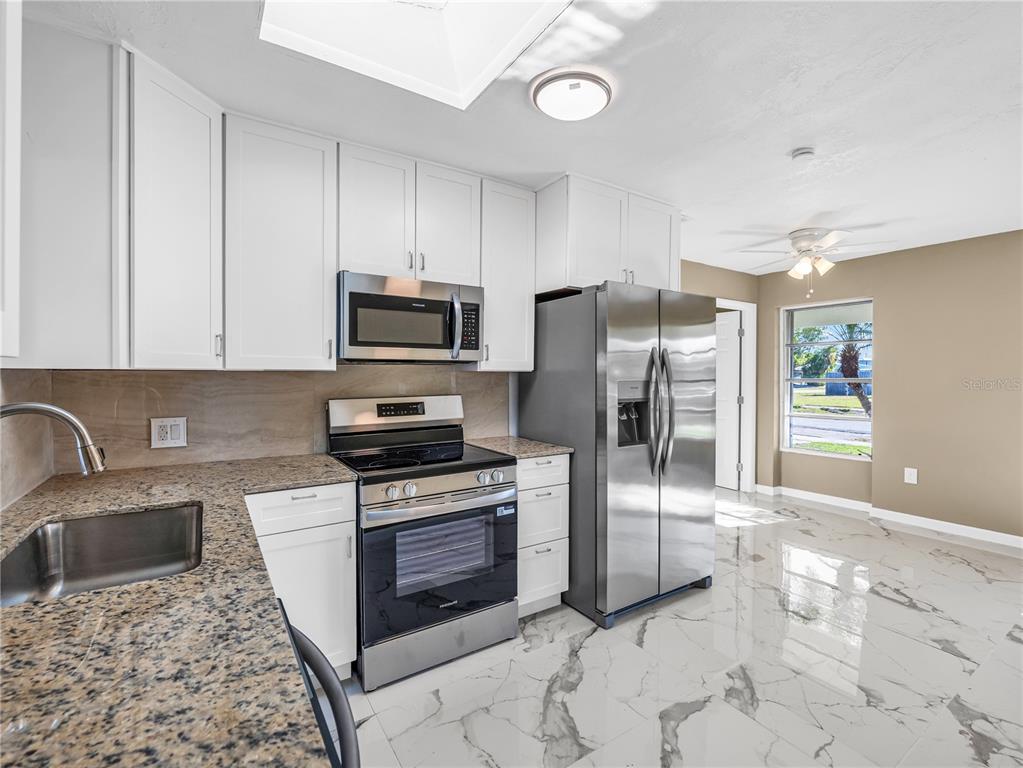 A kitchen features white cabinets, granite countertops, stainless steel appliances, and white marble-look tile flooring — 640 DALTON BOULEVARD, PORT CHARLOTTE, FL