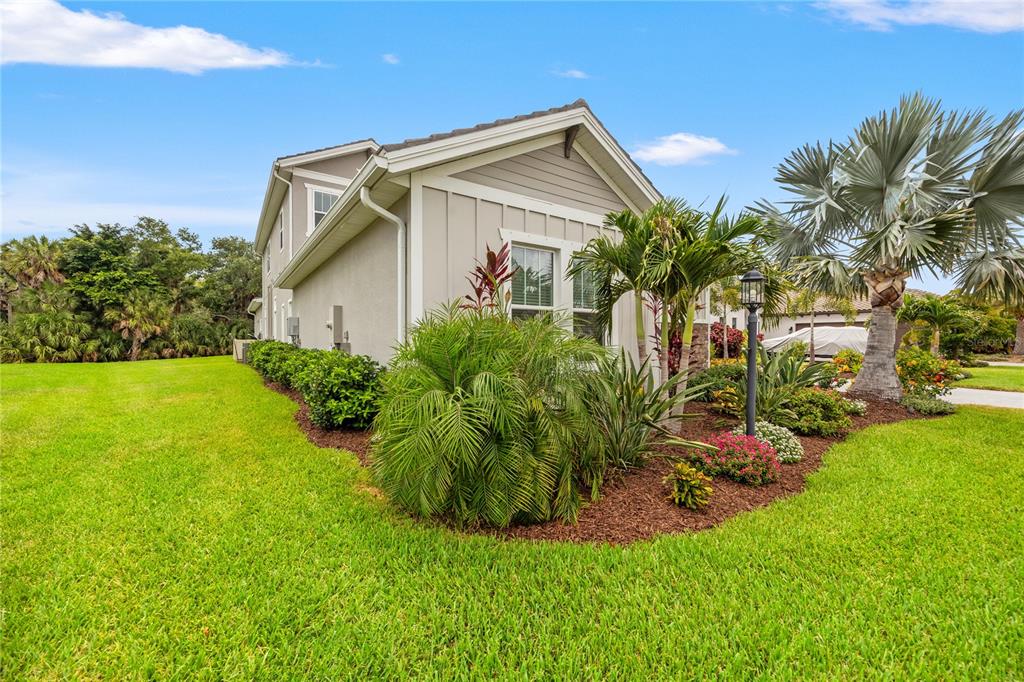 A side view of a beige house with a landscaped garden and a palm tree — 9479 TEQUILA SUNRISE DRIVE, SARASOTA, FL