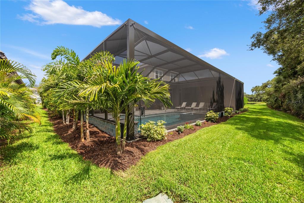 A swimming pool enclosed by a screened lanai sits in a backyard with palm trees — 9479 TEQUILA SUNRISE DRIVE, SARASOTA, FL