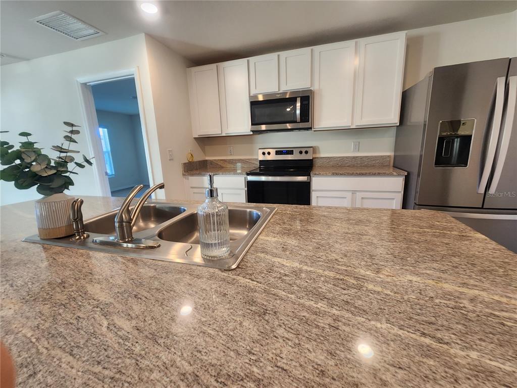 A kitchen features granite countertops, white cabinetry, stainless steel appliances, and a central island sink — 8696 SW 49TH CIRCLE, OCALA, FL